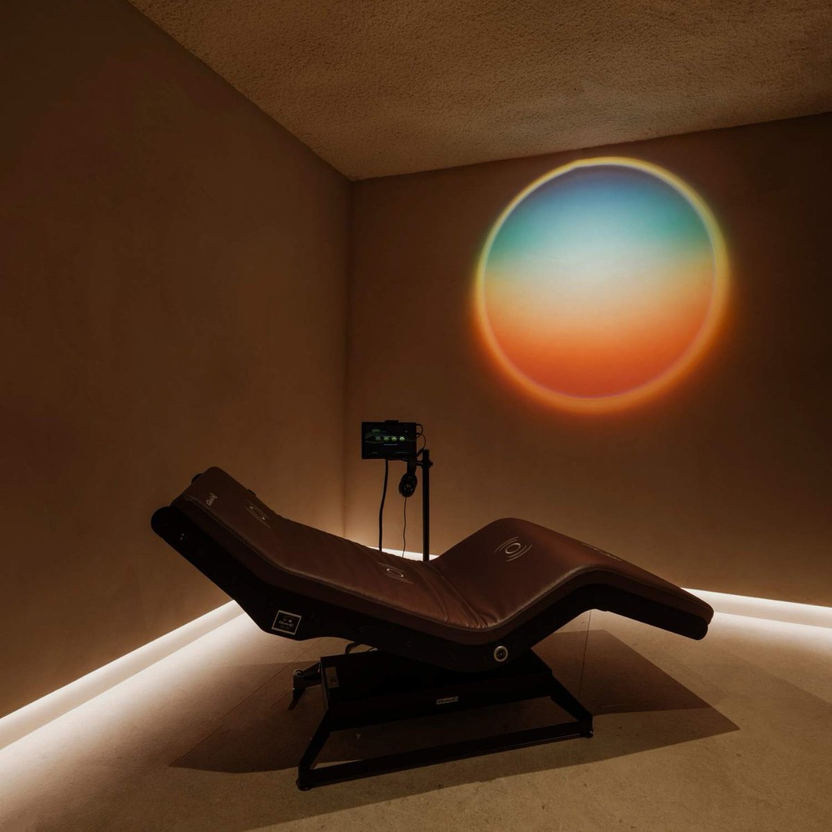 A vibroacoustic lounger in a dim treatment room at Nao, with a circle of coloured light on the wall