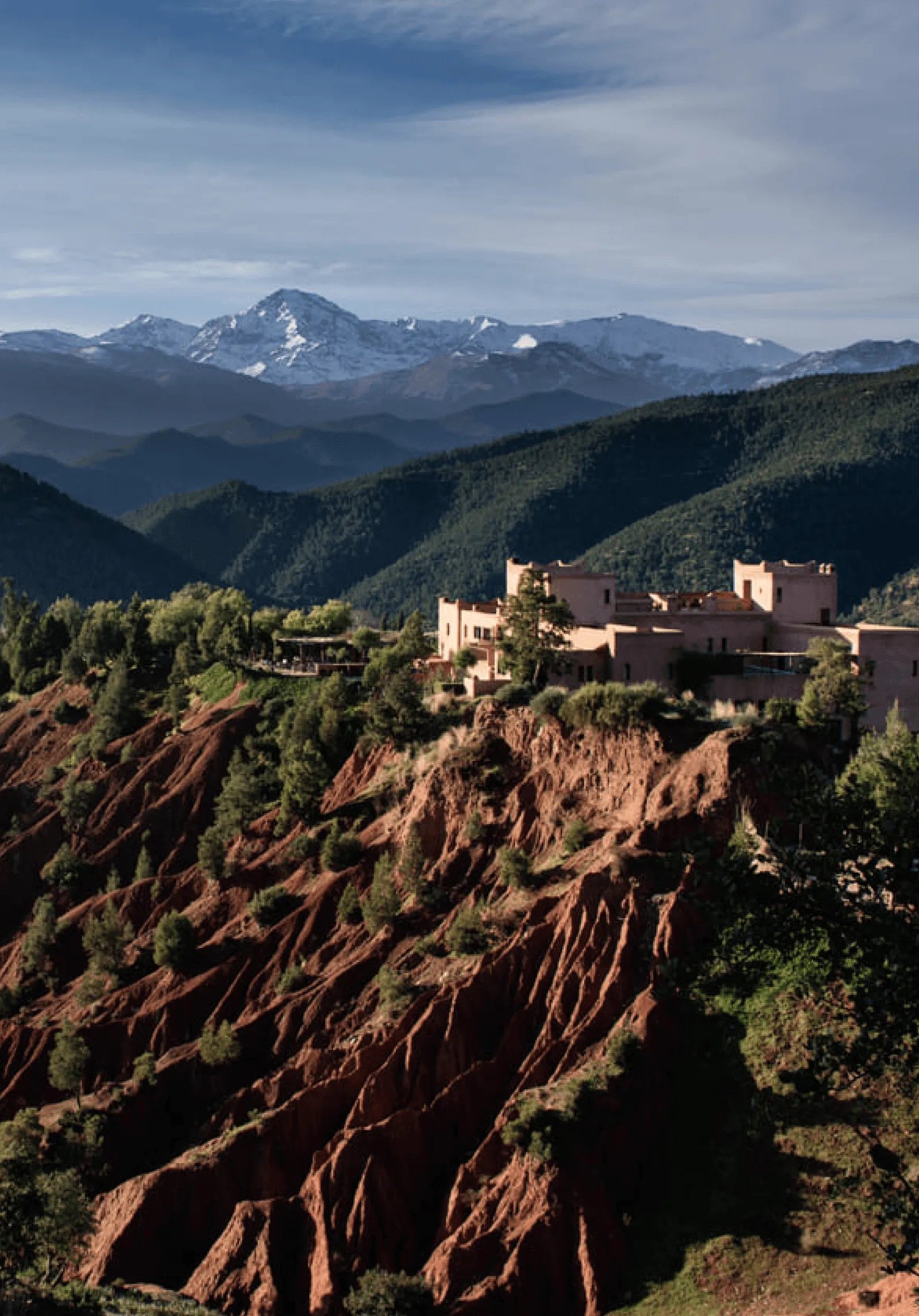 Kasbah Bab Ourika on a red-earth hilltop above the Ourika Valley, the snow-capped High Atlas behind