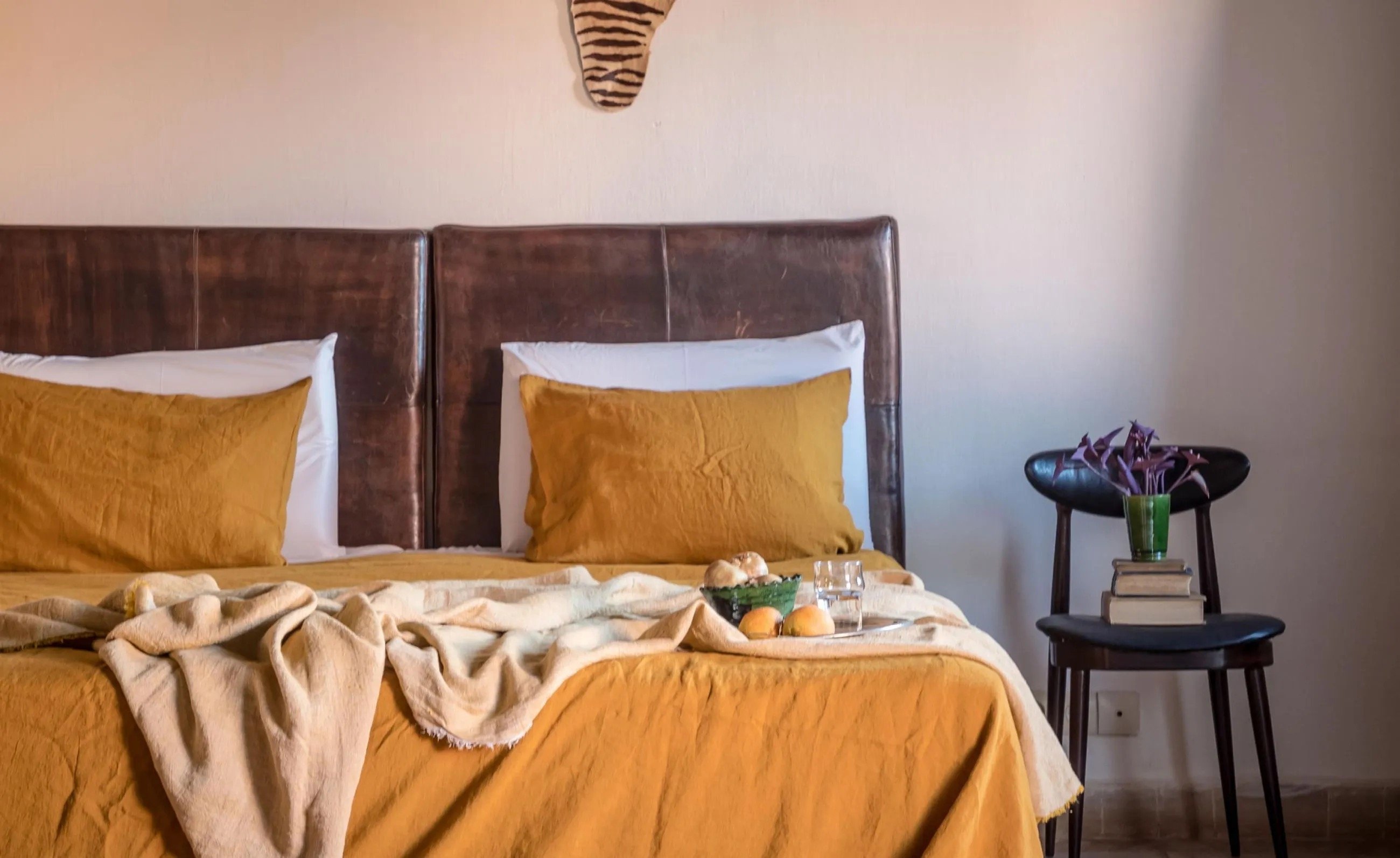 A guest room with ochre linen, a leather headboard and a Berber side table