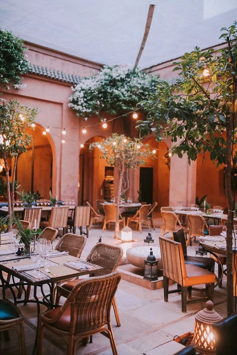 The courtyard restaurant at dusk, hung with lanterns and rattan chairs on rose-earth walls