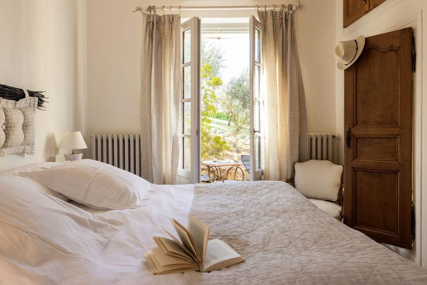 A guest room with white linen and French doors open to the olive trees