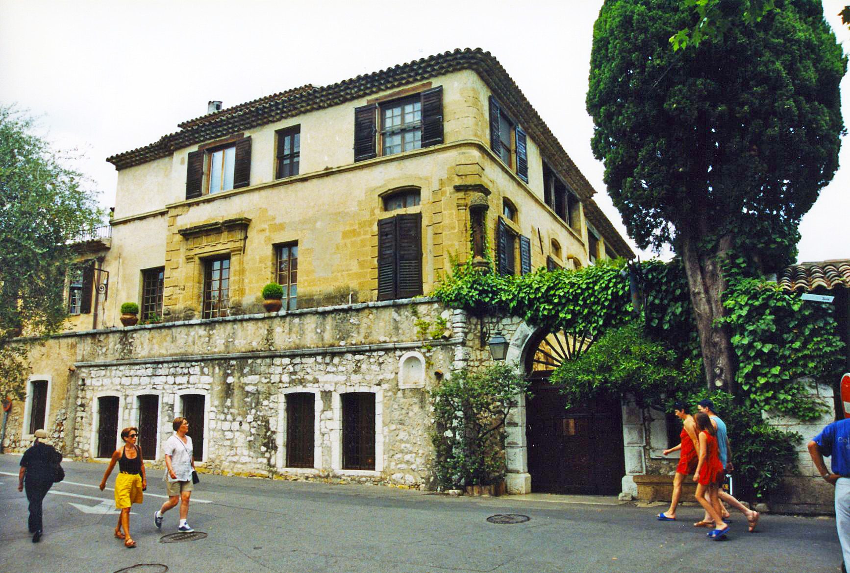 The ochre facade of La Colombe d'Or with green shutters, ivy and a cypress, at the gate of Saint-Paul-de-Vence