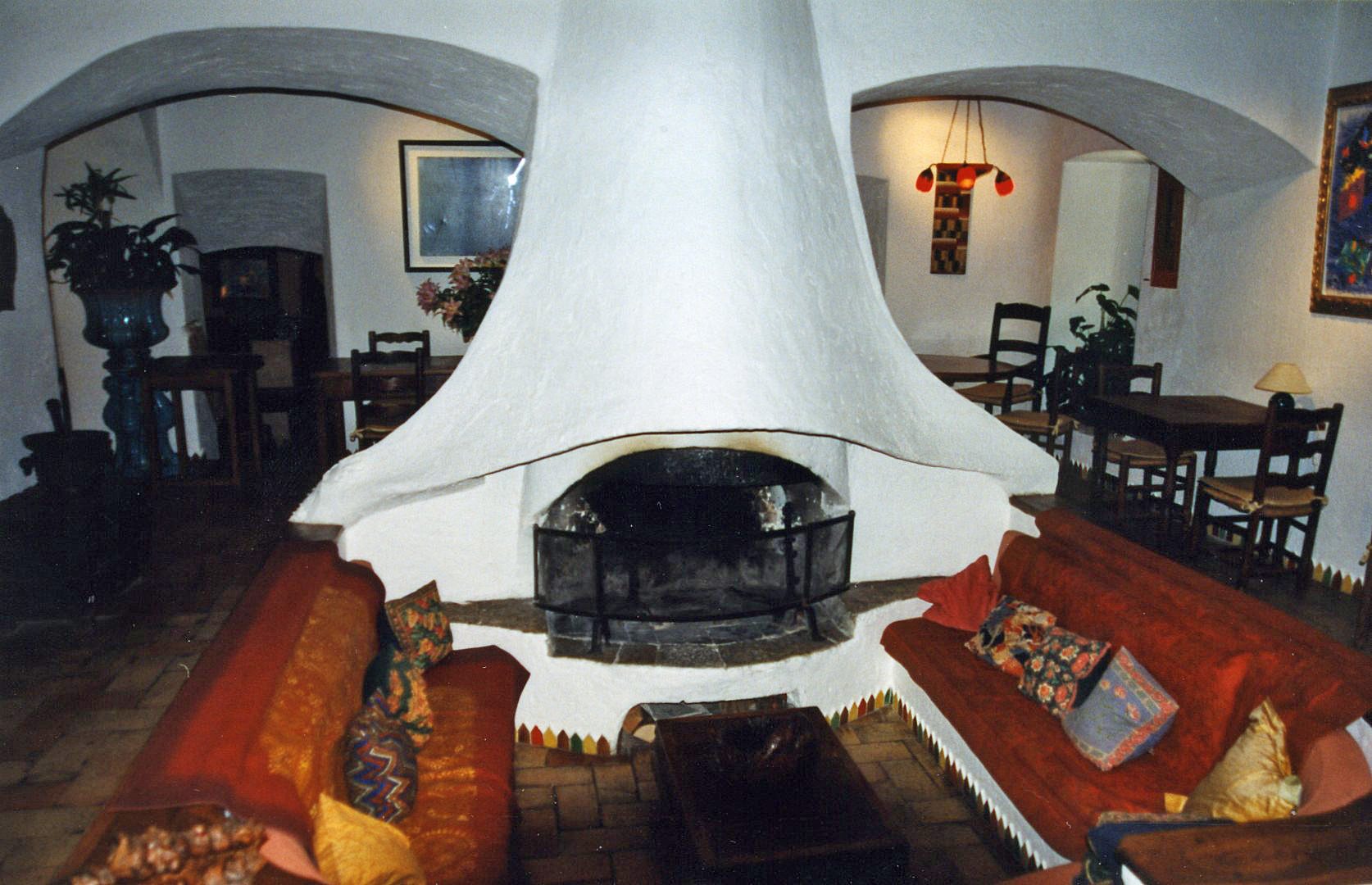The vaulted salon with its white central fireplace, deep red sofas and a painting on the wall