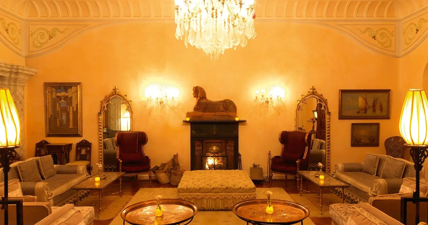The grand salon under a crystal chandelier, antiques and a carved sphinx above the fireplace