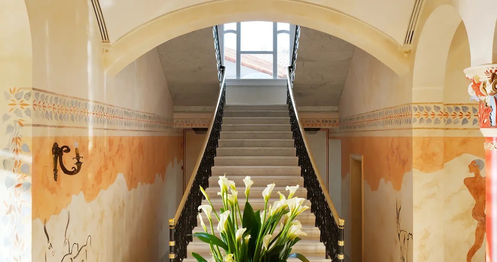 A marble staircase rising past walls painted with Minoan-style murals