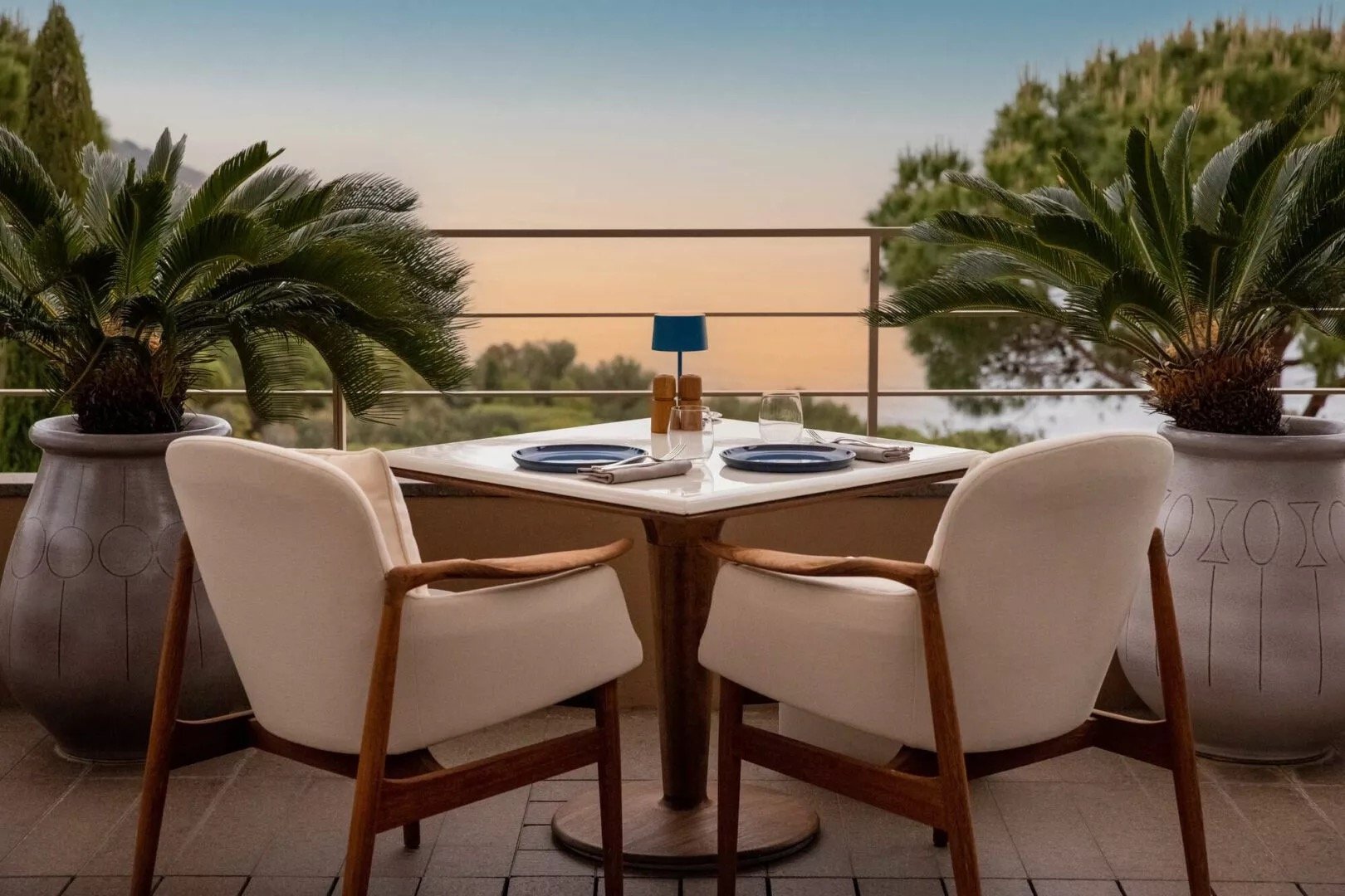 A table for two on the terrace at dusk, framed by potted palms