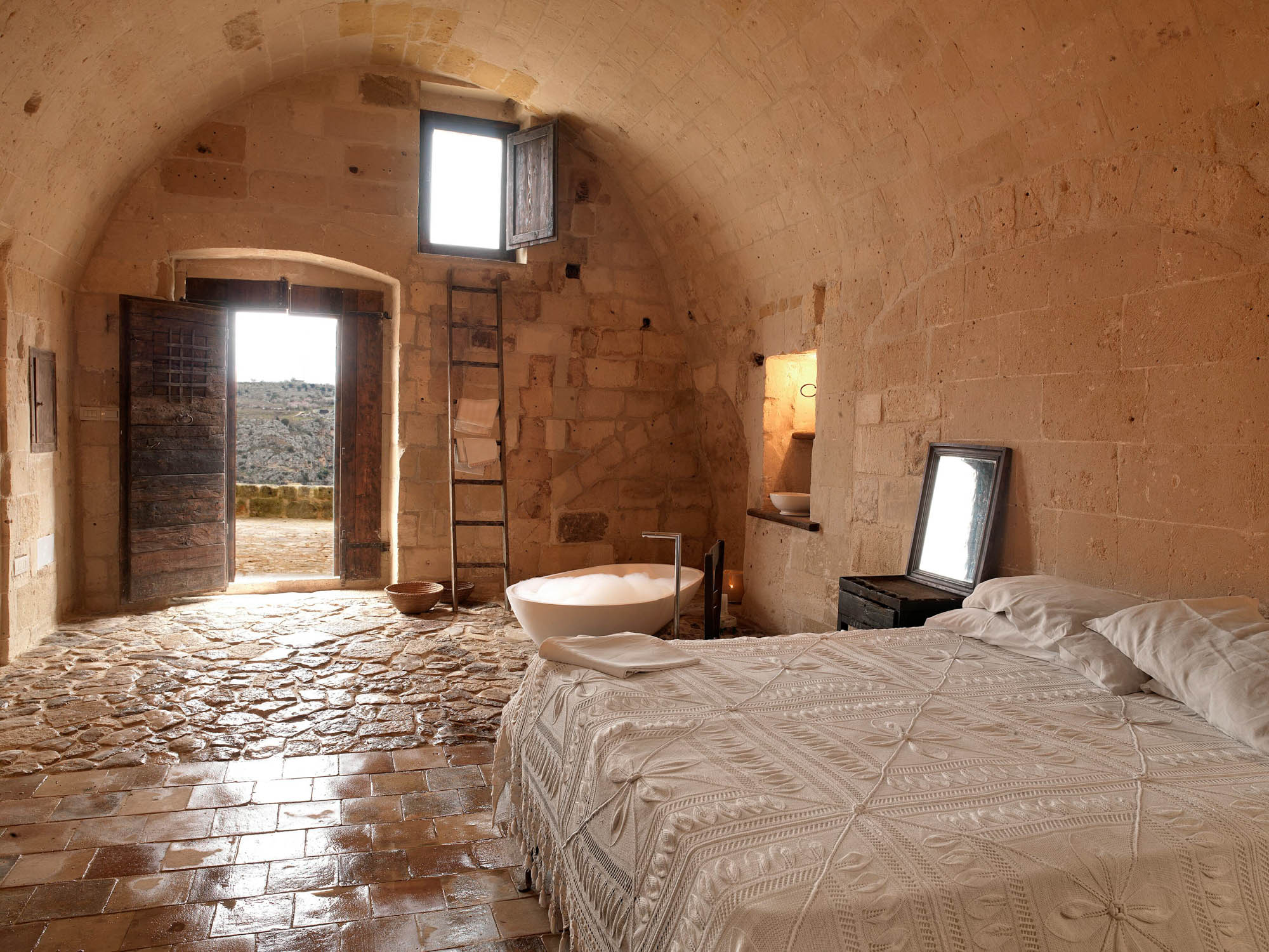 A vaulted cave room with a stone floor and a door open to the Murgia