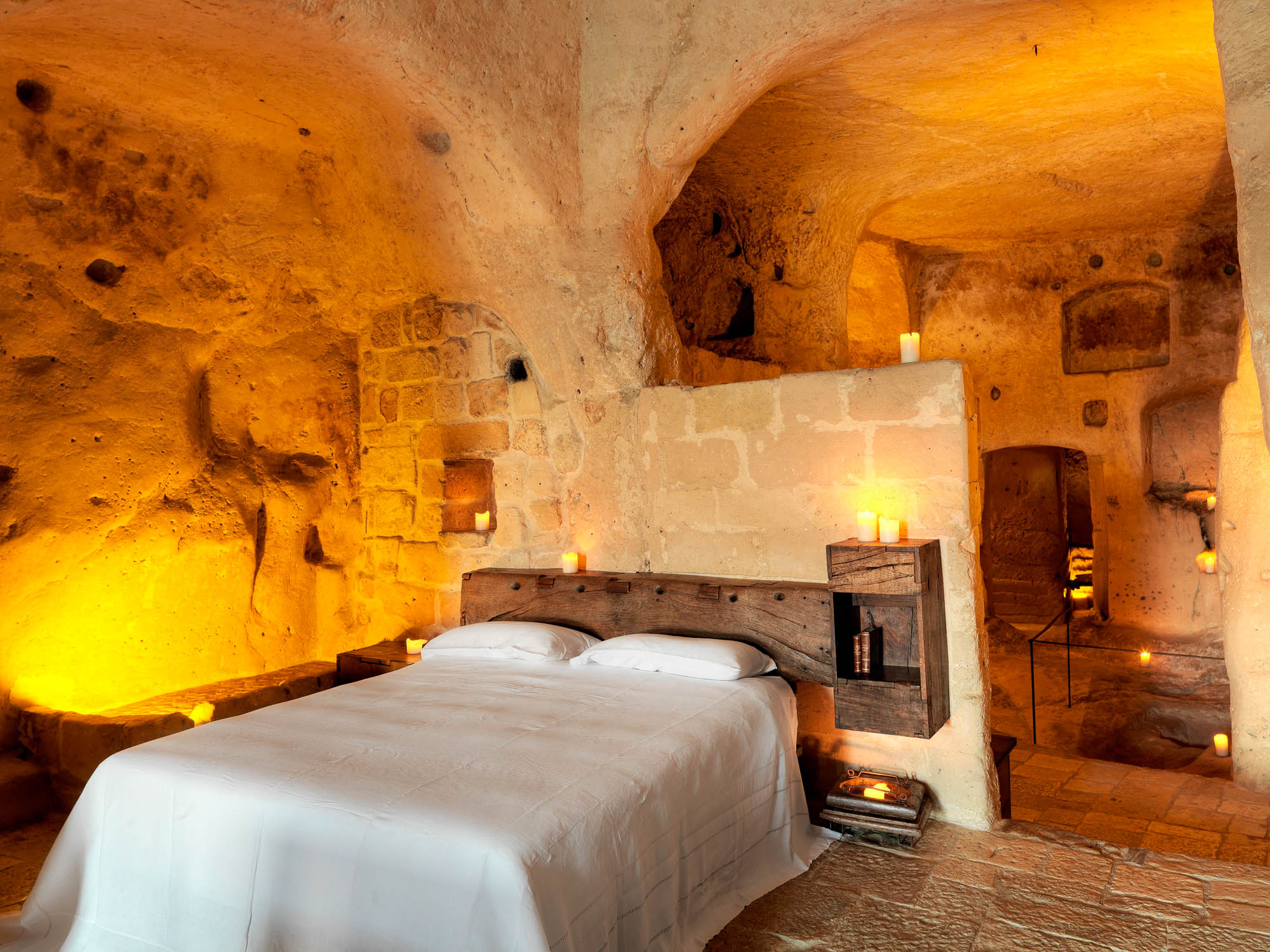 A cave room lit by candlelight, the bed set against carved rock