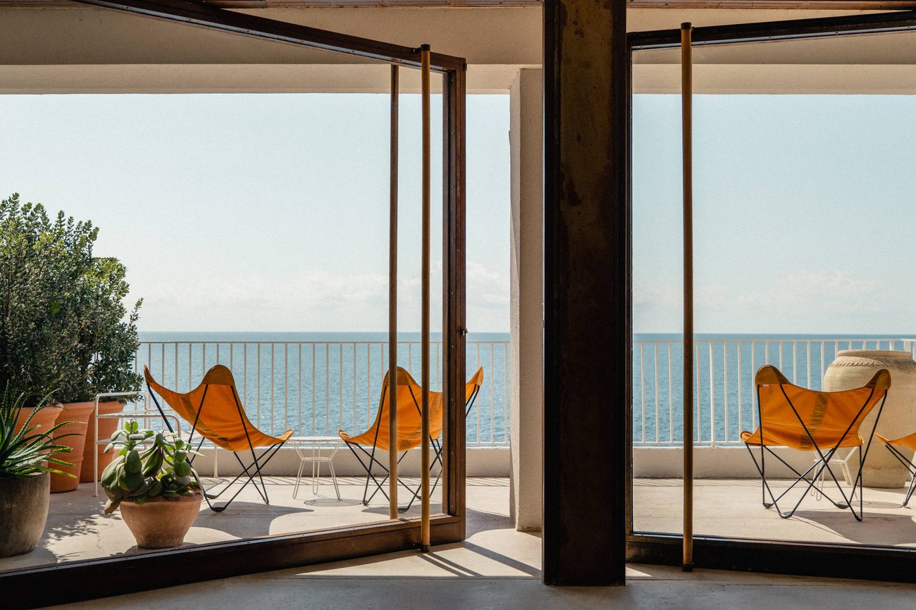 An interior lounge with butterfly chairs framing the Mediterranean through full-height windows