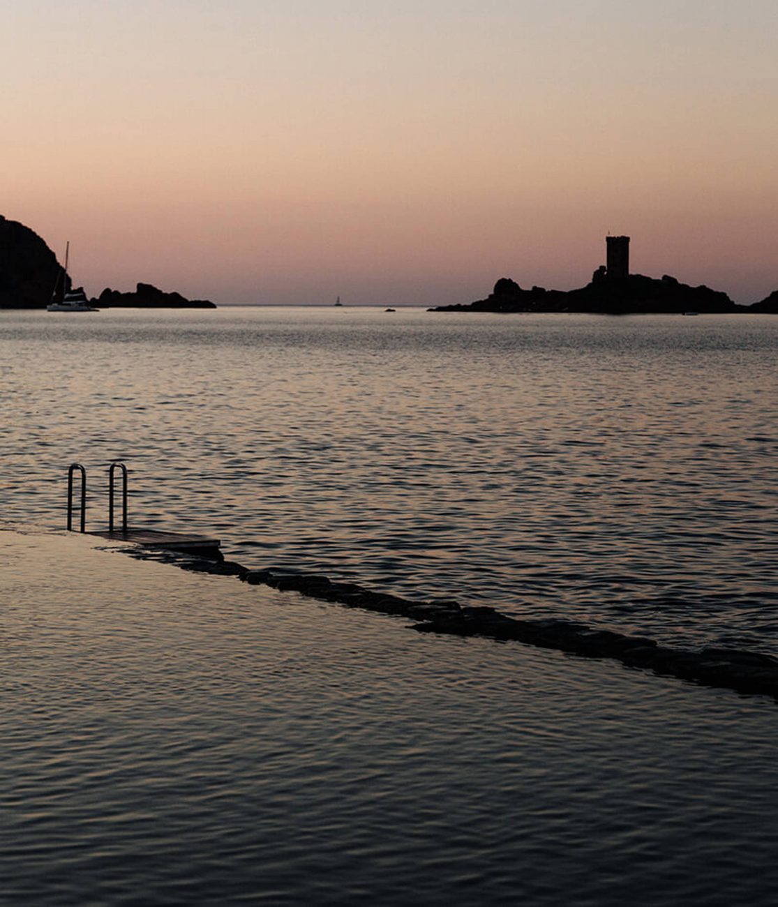 Dusk over the sea with the tower of the Île d'Or and the pool's edge in silhouette