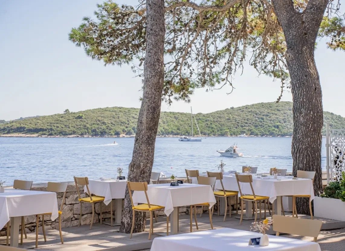 The restaurant terrace by day under pines, tables above the sea
