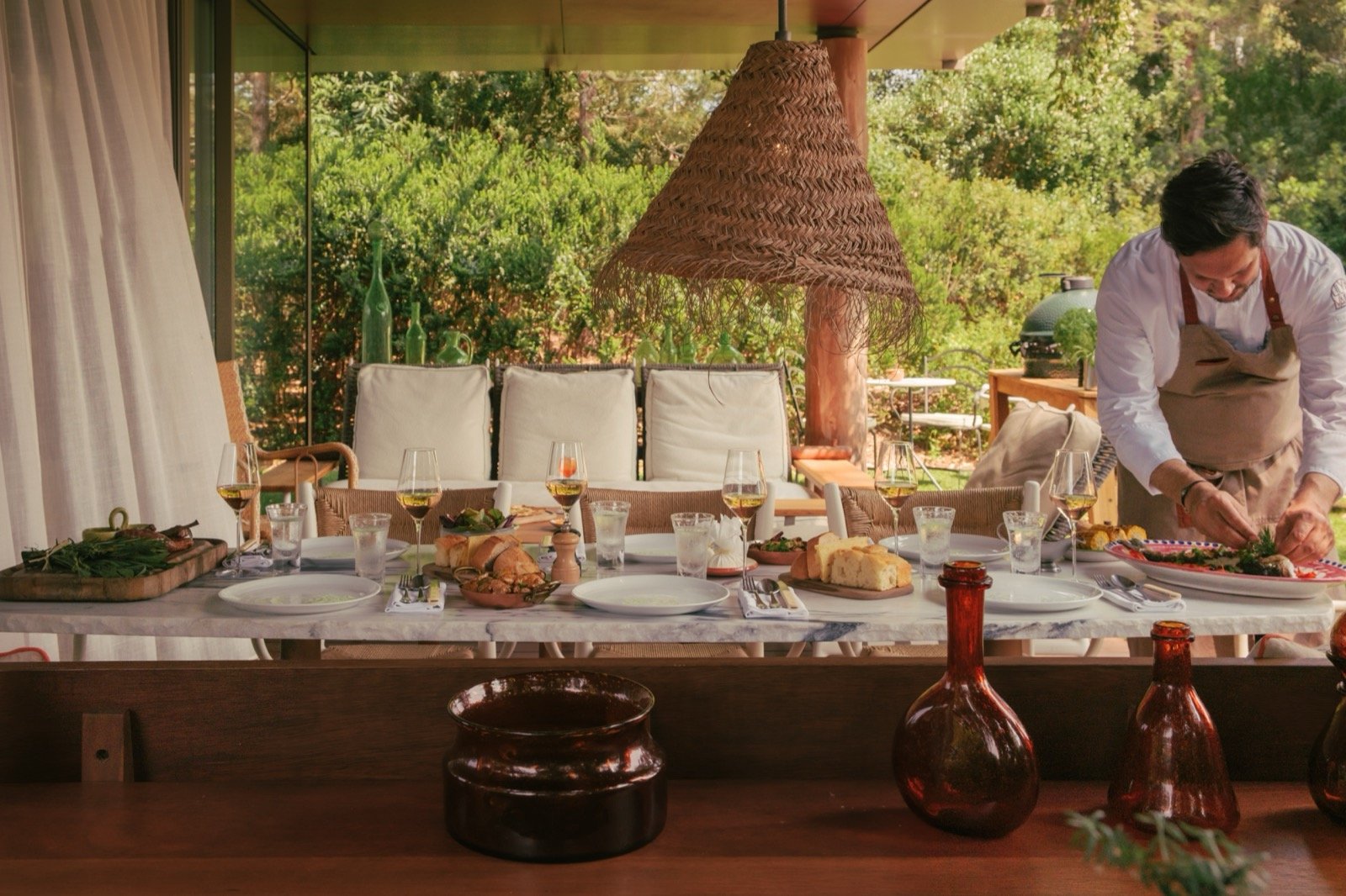 A chef finishing plates at a long table under the pergola