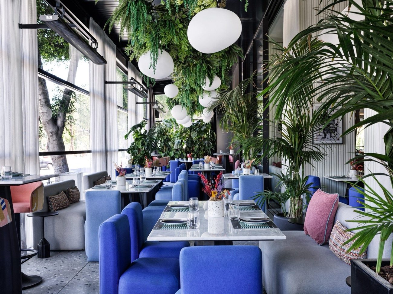 Scale restaurant with blue velvet banquettes, marble tables and a canopy of hanging greenery