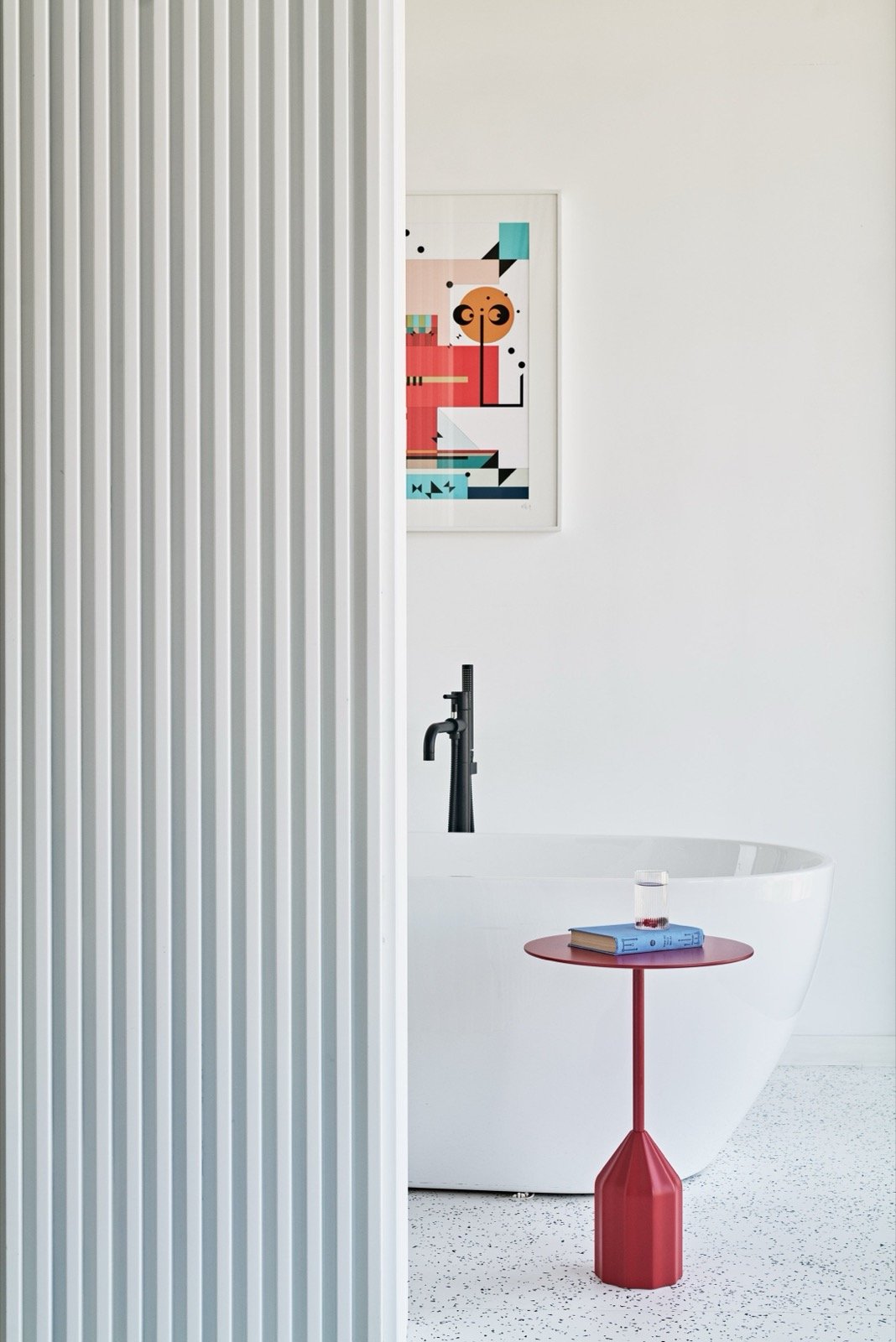 A suite bathroom with a freestanding tub, black fittings and a framed geometric print