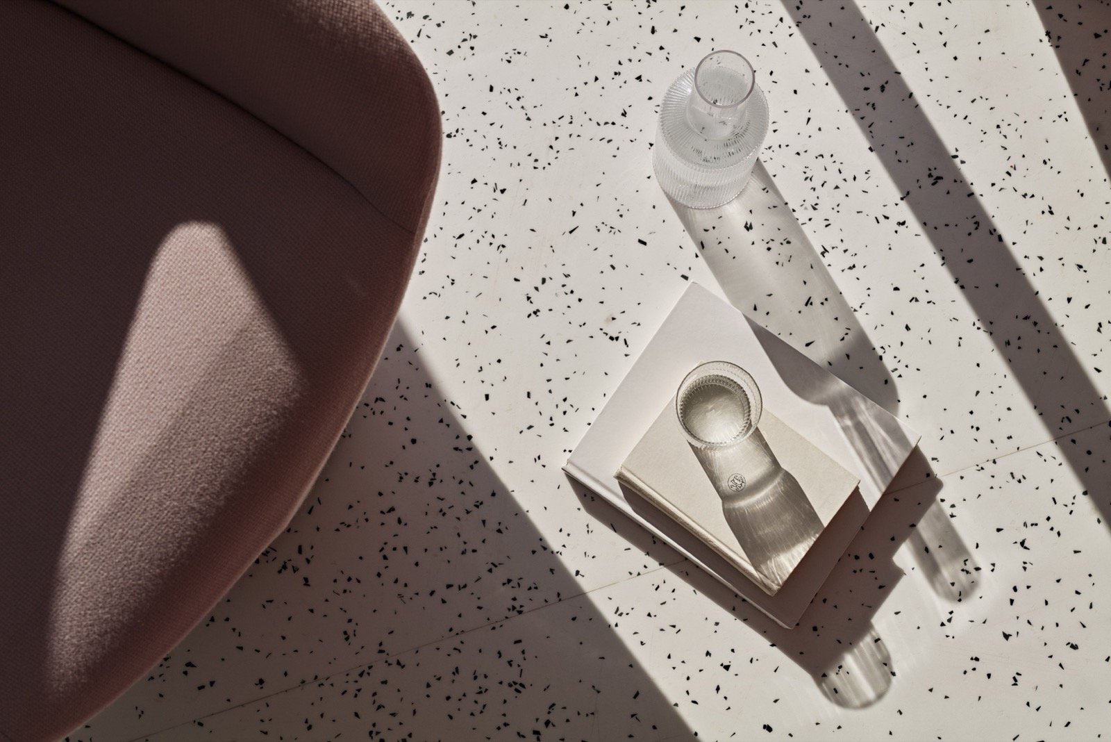 A design detail, a ribbed glass carafe and tumbler on a terrazzo surface in low sun