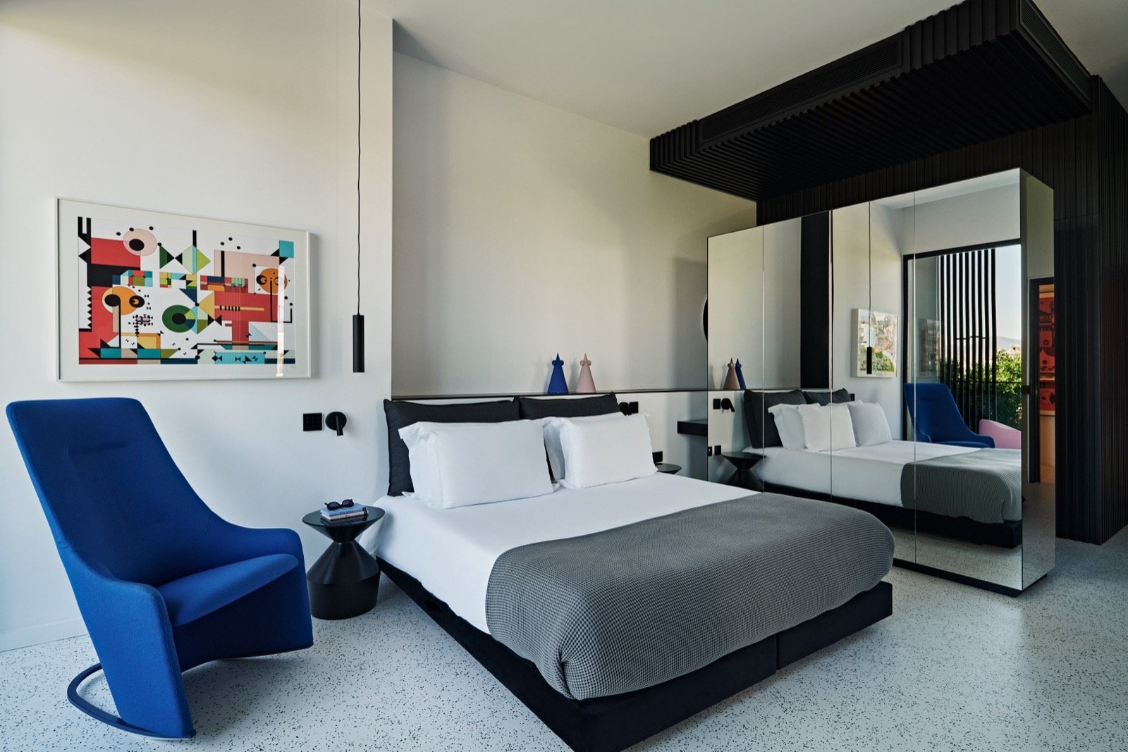 A Junior Suite with a cobalt lounge chair beneath a bold geometric artwork