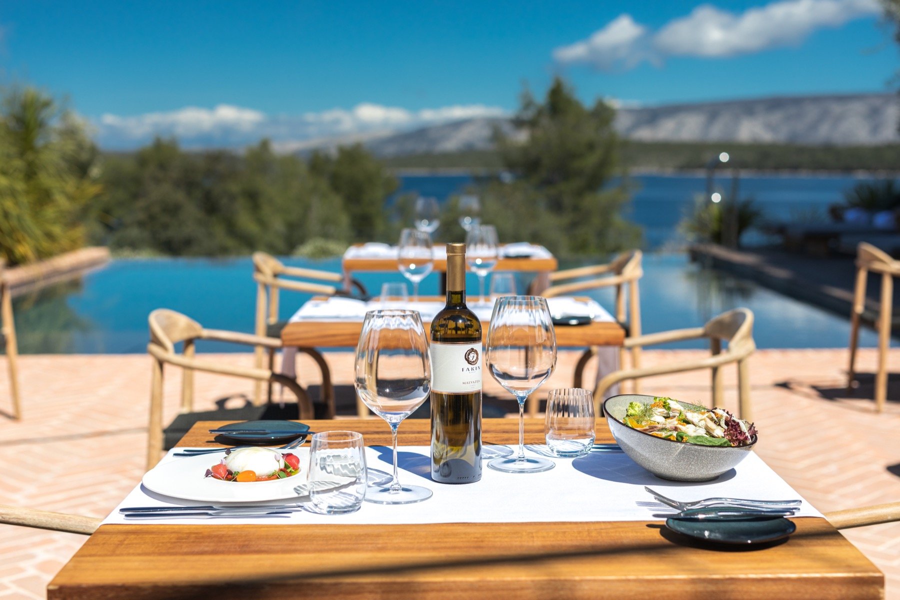 A table laid by the pool with the bay and hills beyond