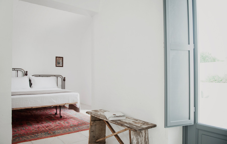 A guest room with an iron bed, a kilim and pale shutters