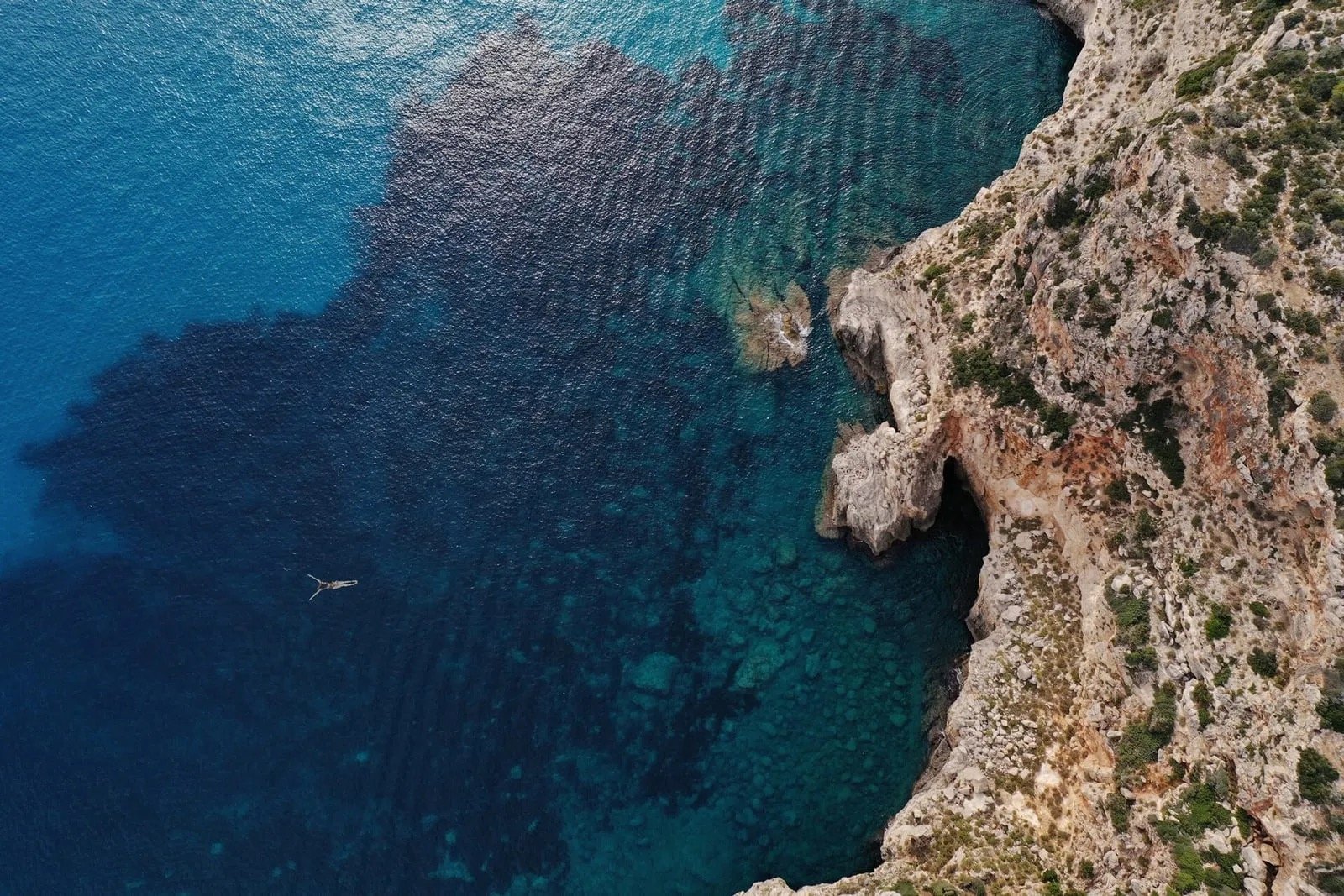 A swimmer in the clear water below the cliffs of the island's south coast
