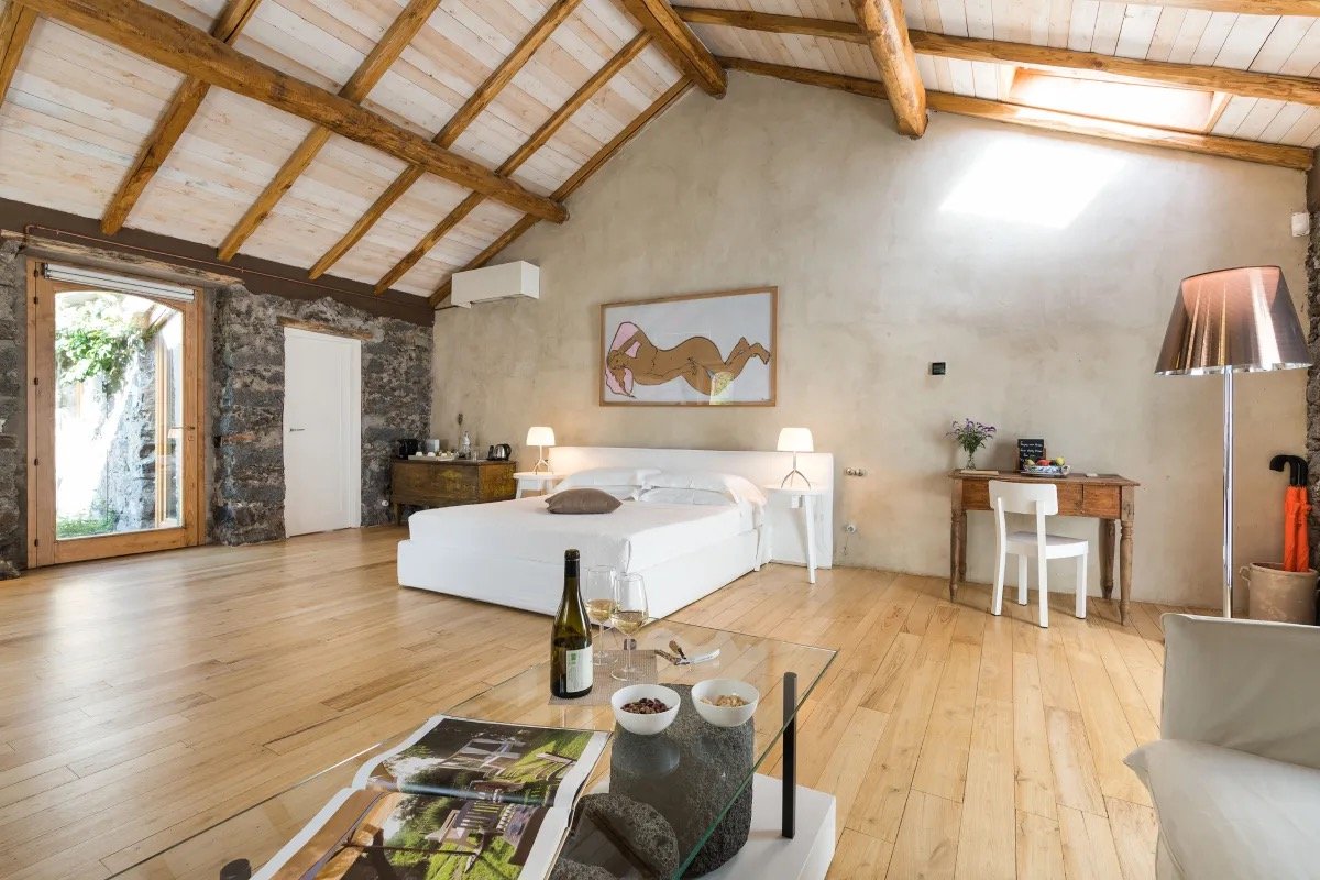 A suite under chestnut beams, with lava-stone walls and pale wooden floors