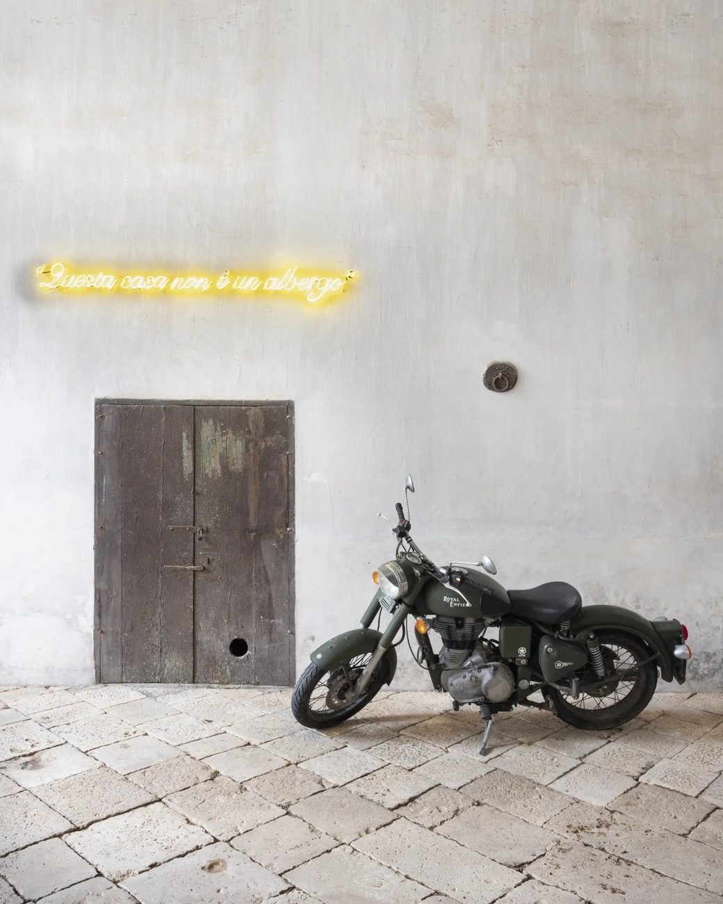 A neon reading Questa casa non è un albergo above a courtyard door