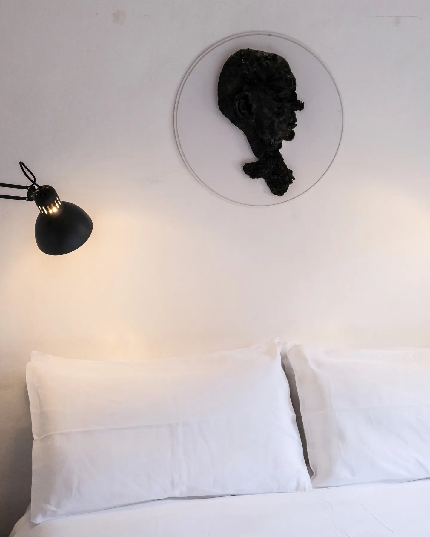A plain white bed below a cast bronze head