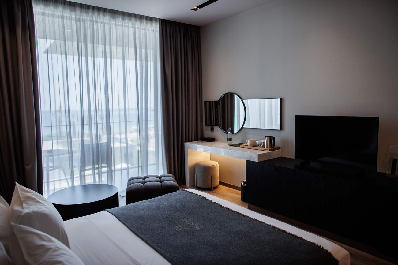 A room in warm greys and wood with floor-to-ceiling glass onto a sea-view balcony
