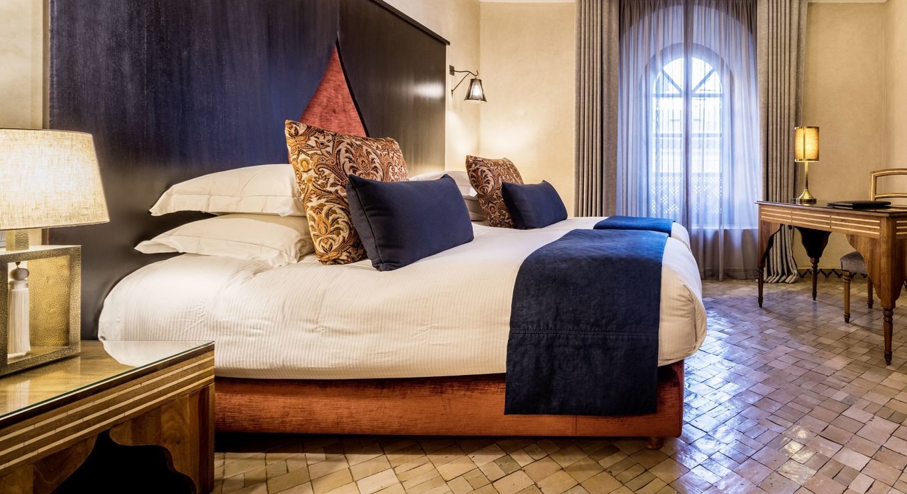 A guest room with a carved headboard and a zellij-tiled floor