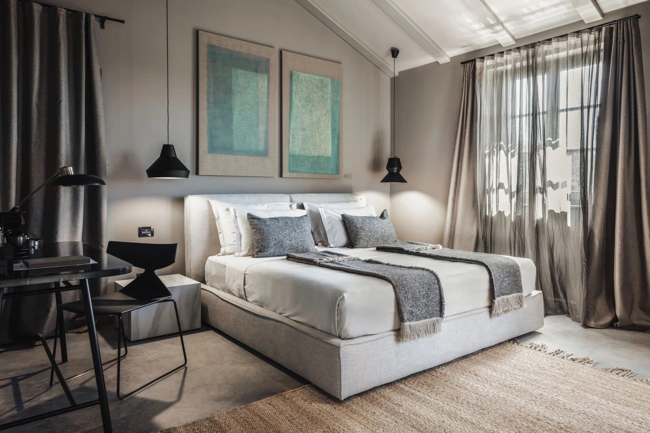 A guest room in calm, neutral tones with a large bed and soft daylight