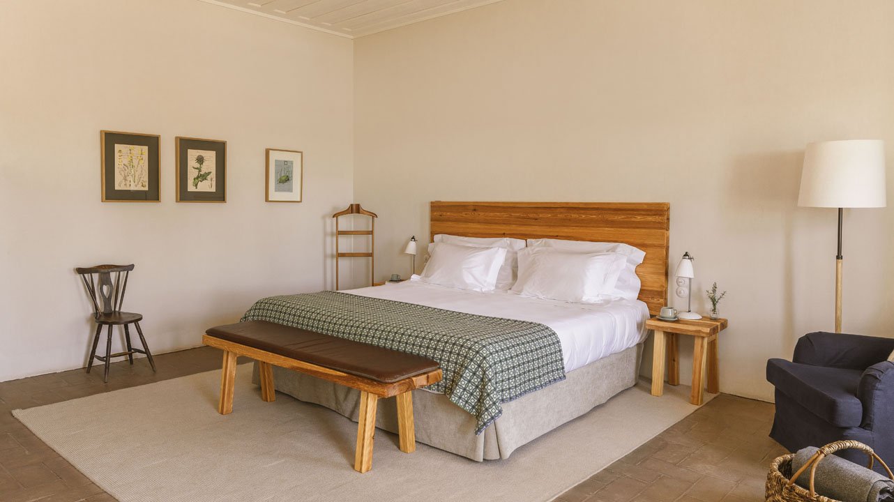 A farm room with lime-washed walls, an oak headboard and botanical prints