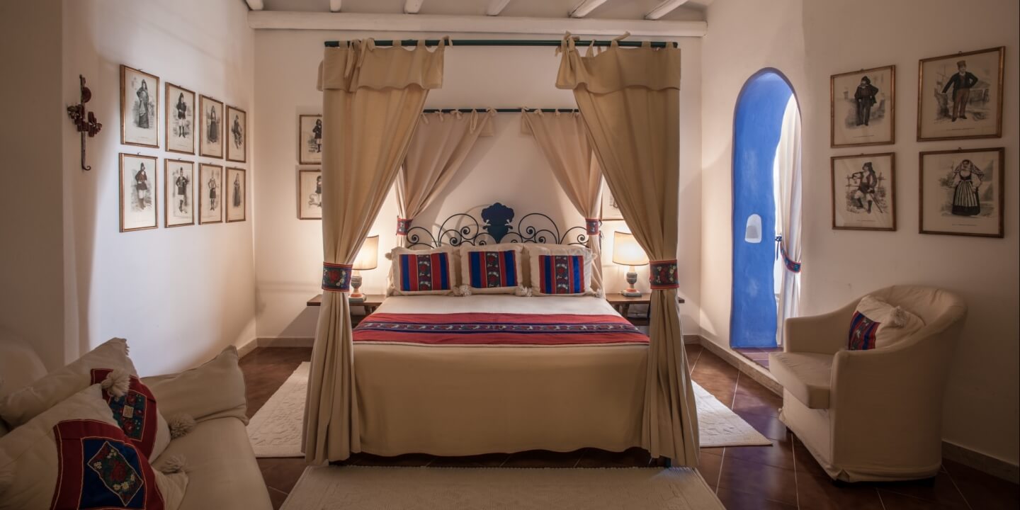 An art junior suite with a canopy bed, whitewashed walls and framed prints of Sardinian costume
