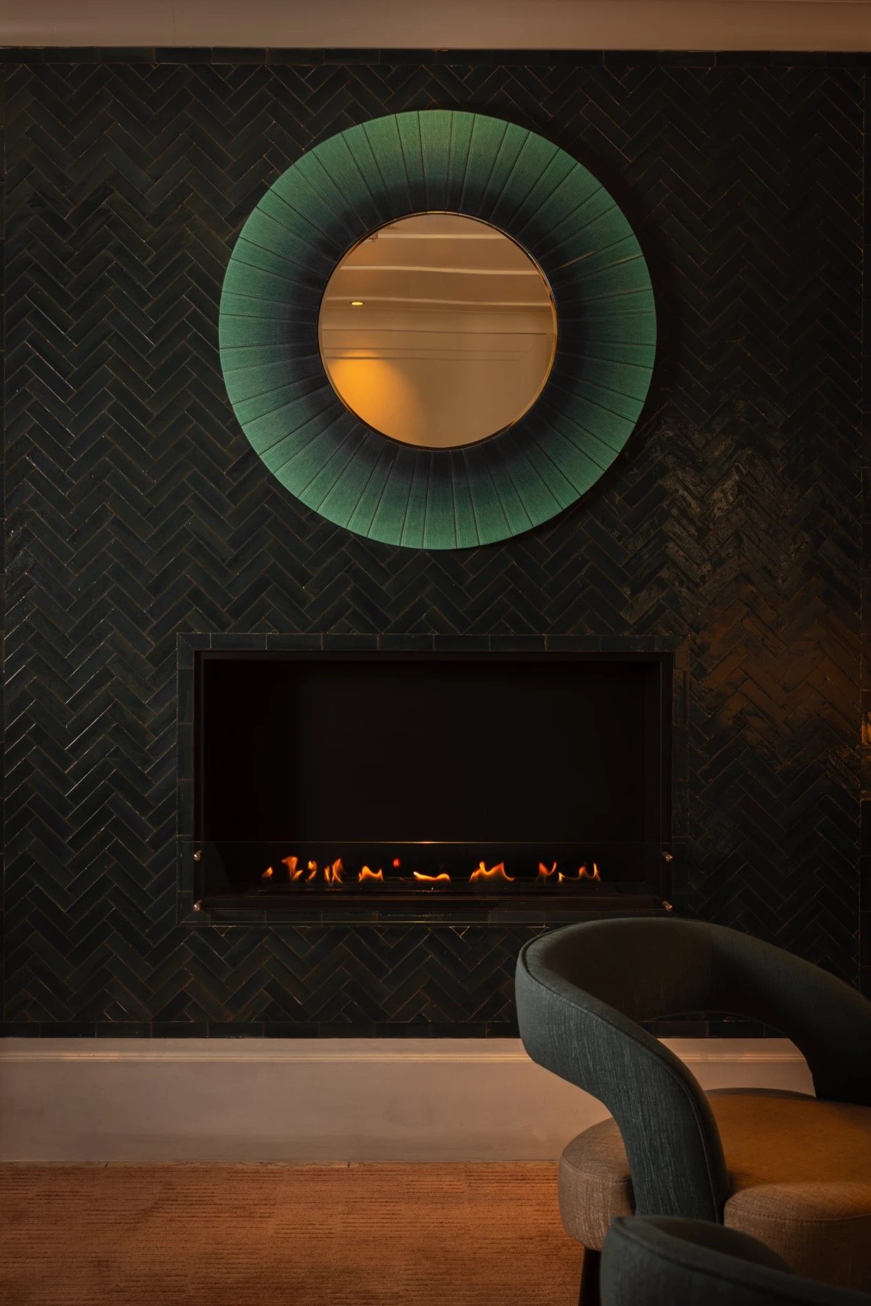 A lounge with a fireplace and round mirror in the estate's low-lit, tactile style