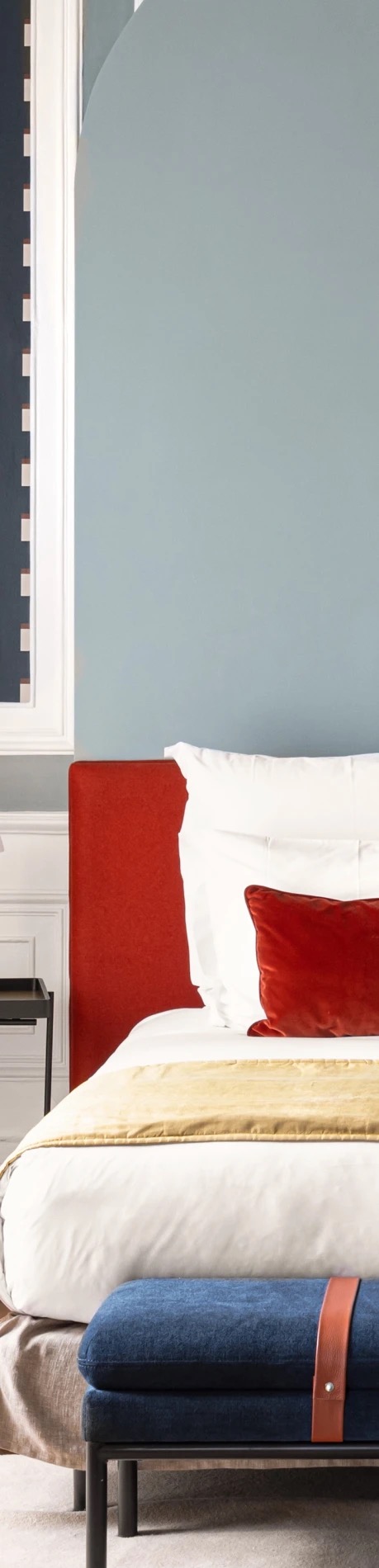 A bedroom in raw wood and linen with a red accent against pale walls