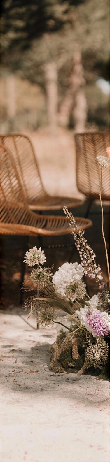 An outdoor table set under the pines with wild flowers and rattan chairs
