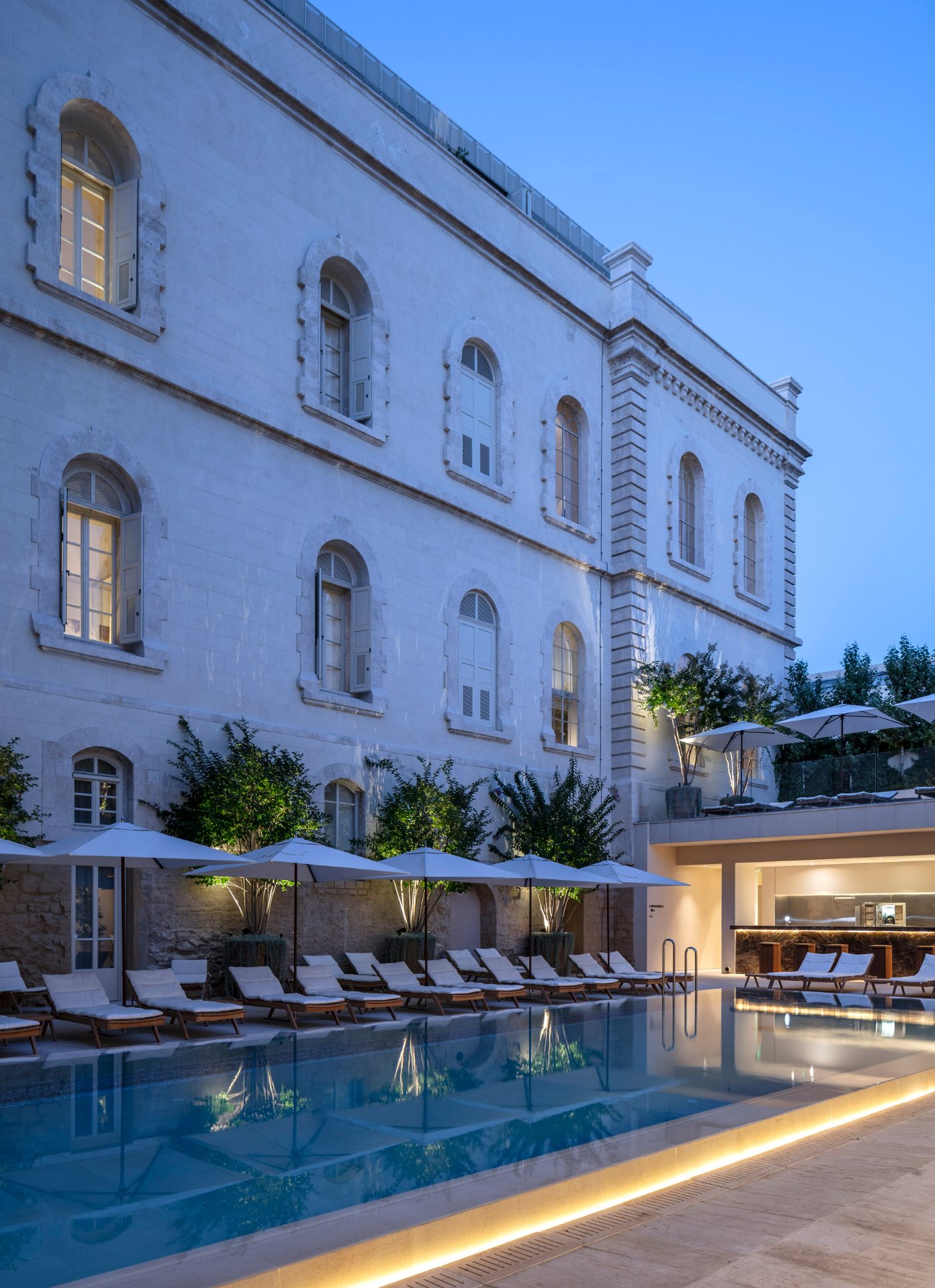 The restored nineteenth-century stone facade above the courtyard pool at dusk