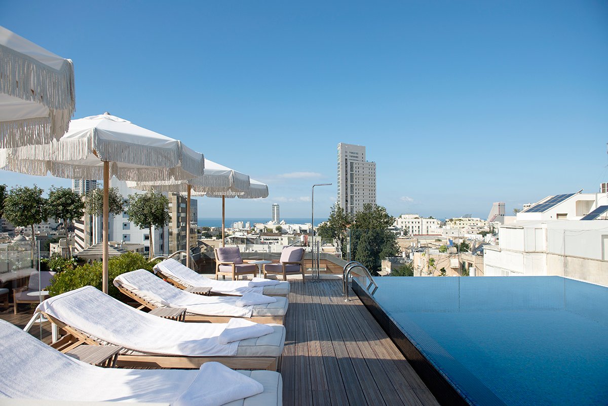 The rooftop pool and loungers with the Tel Aviv skyline and a line of sea beyond
