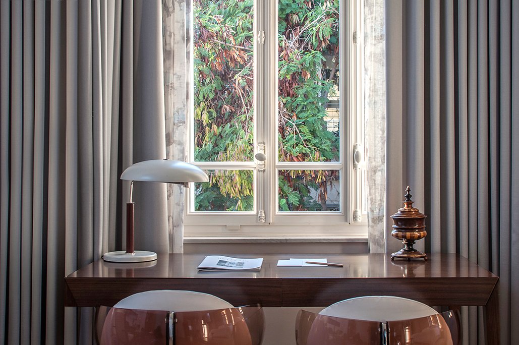 A room desk beneath a tall shuttered 1920s window with a mid-century lamp