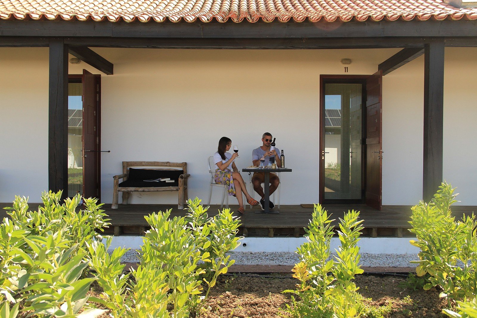 A guest room opening onto a shaded veranda with greenery beyond