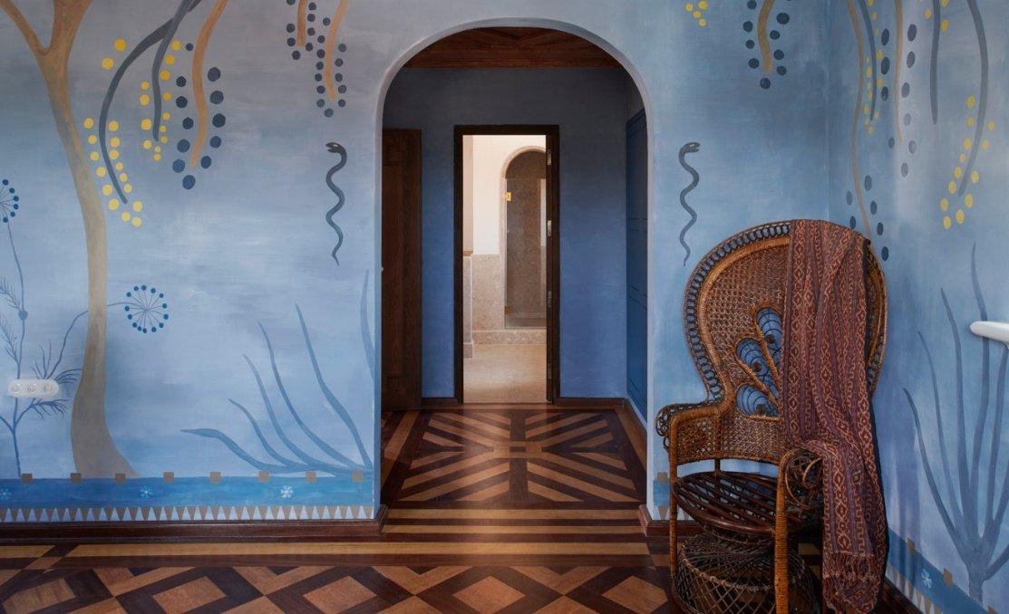 A guest room wall hand-painted with a blue fresco, over parquet floors