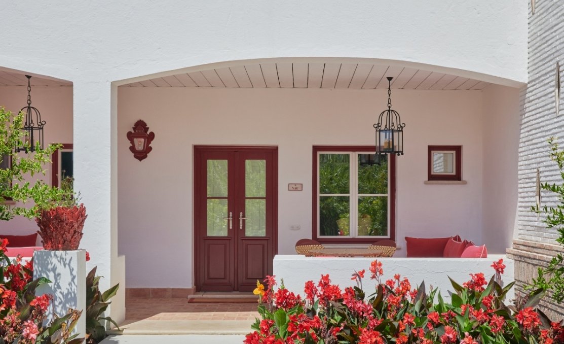 A guest room entrance in soft pink, framed by red canna lilies