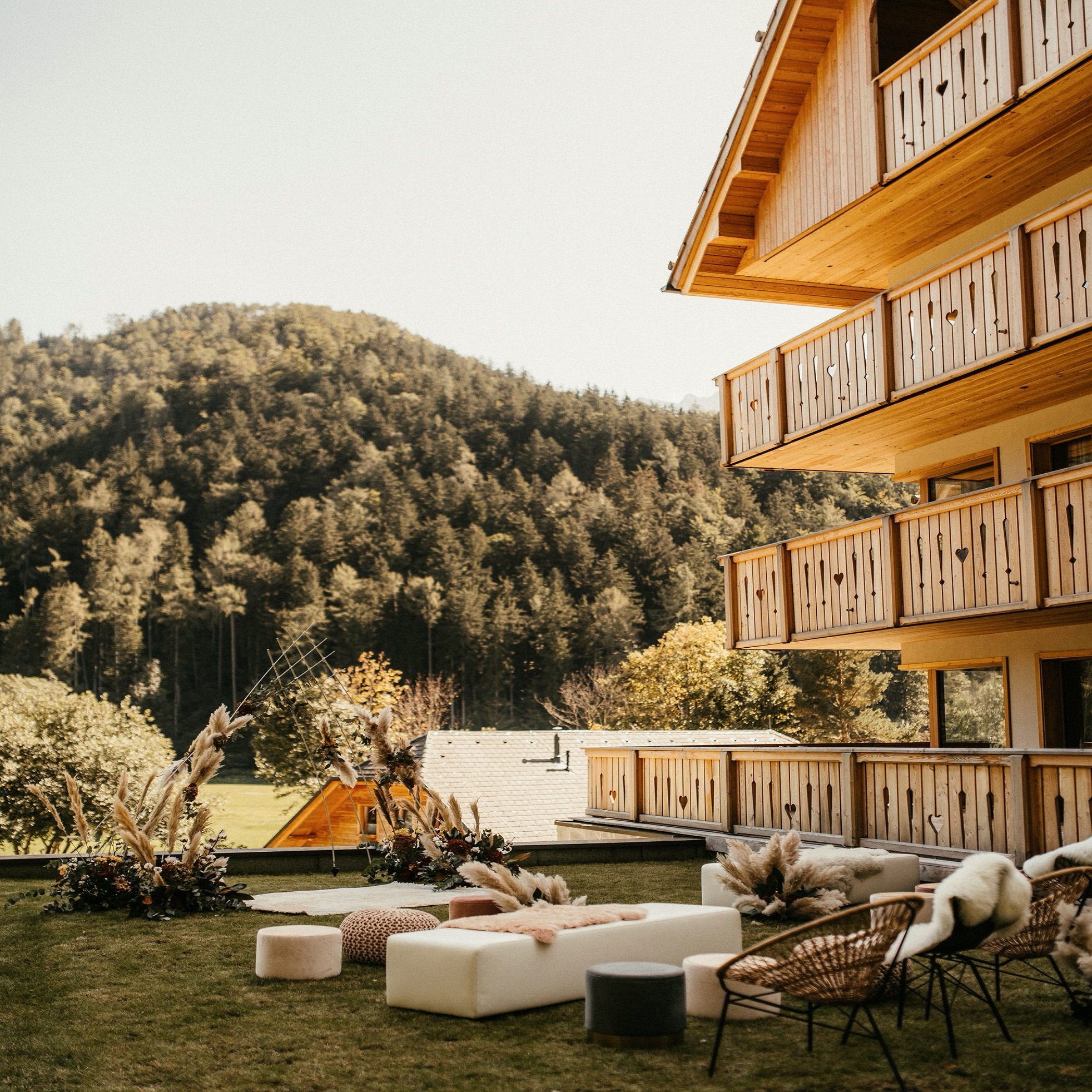 The timber house and its balconies above an outdoor lounge, forested slopes rising behind