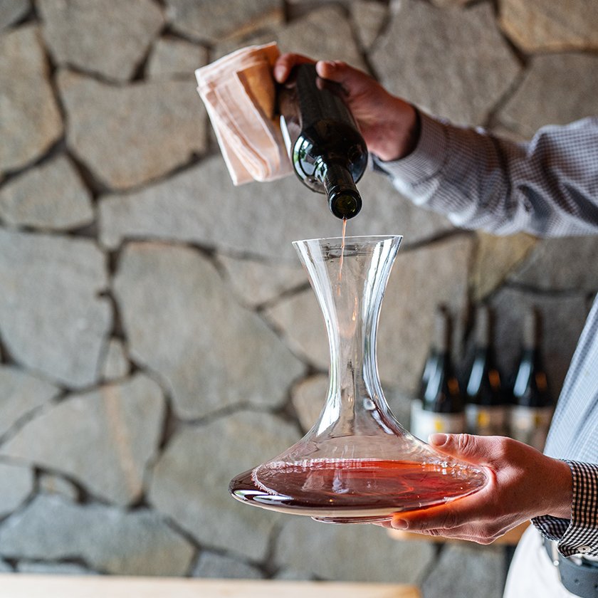 A sommelier decanting red wine against the cellar's stone wall
