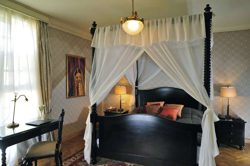 A room with a black four-poster bed under muslin and patterned walls