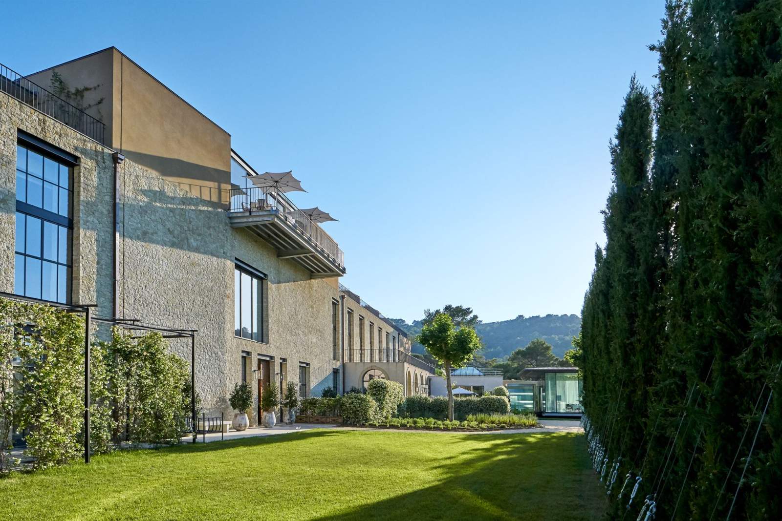 The hotel's stone facade along a cypress hedge and lawn