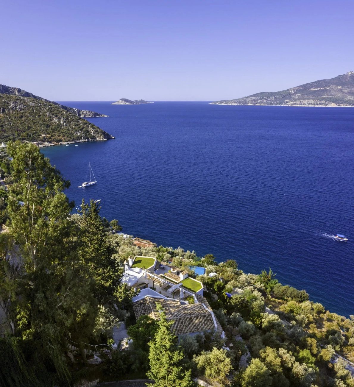 Aerial view of Villa Mahal's white buildings among olive groves above the deep blue bay