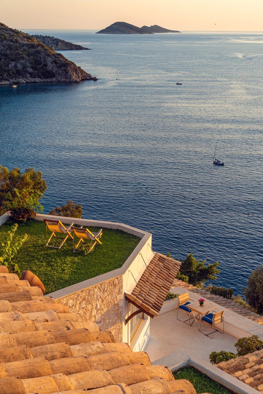 A lawn terrace and sun loungers above the sea at dusk, an island on the horizon