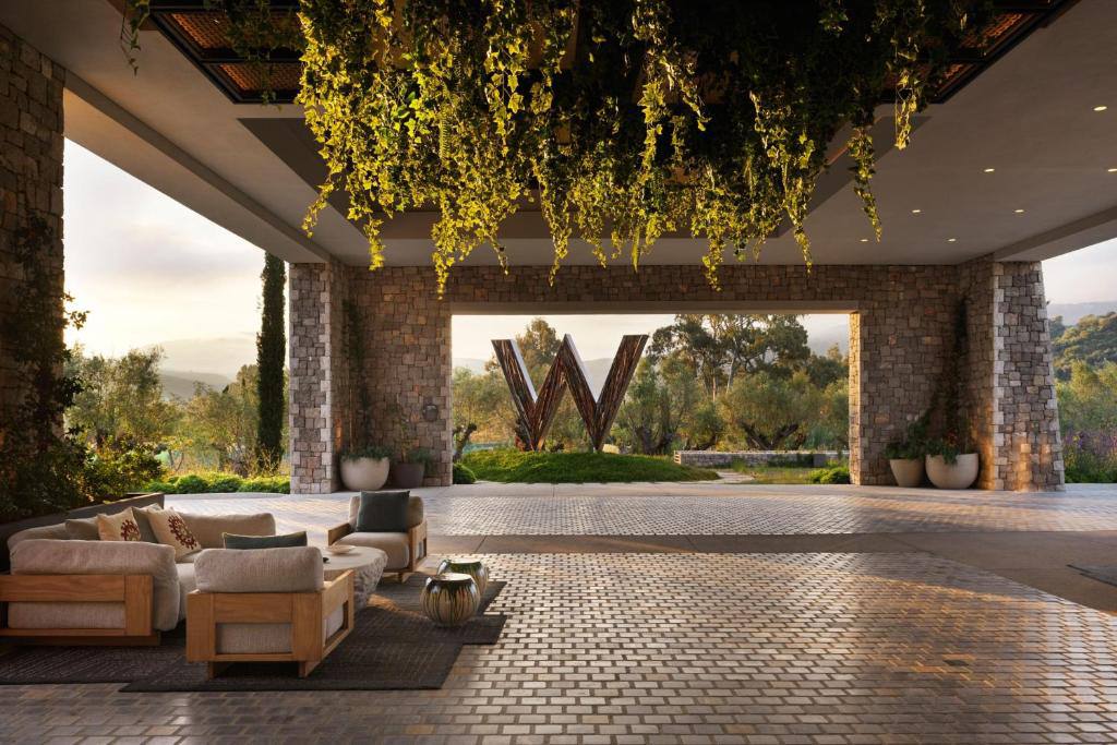 Open-air arrival lounge with the W mark and olive grove at sunset
